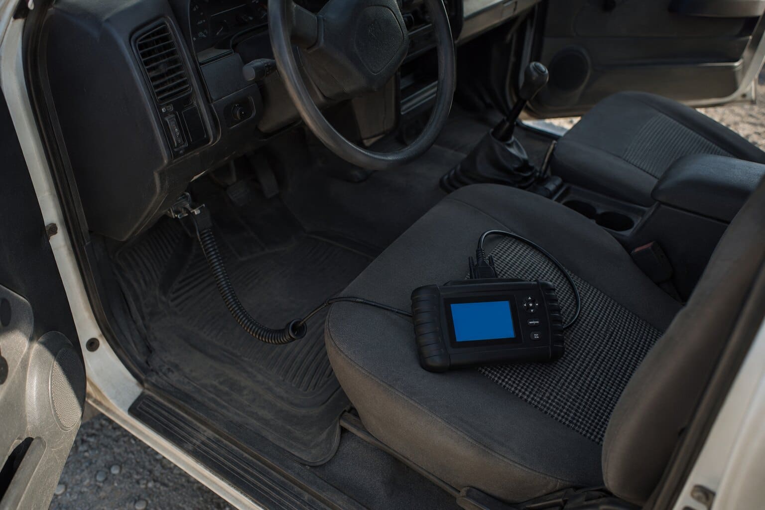 Equipo de diagnóstico portátil apoyado sobre el asiento de una camioneta, con el cable conectado bajo el volante.