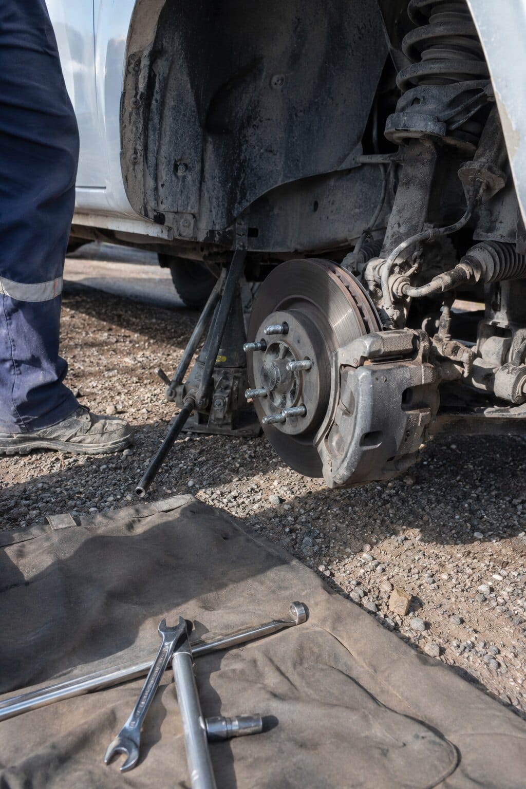 Cambio de pastillas de freno sobre una camioneta levantada con gato, en un camino de ripio.